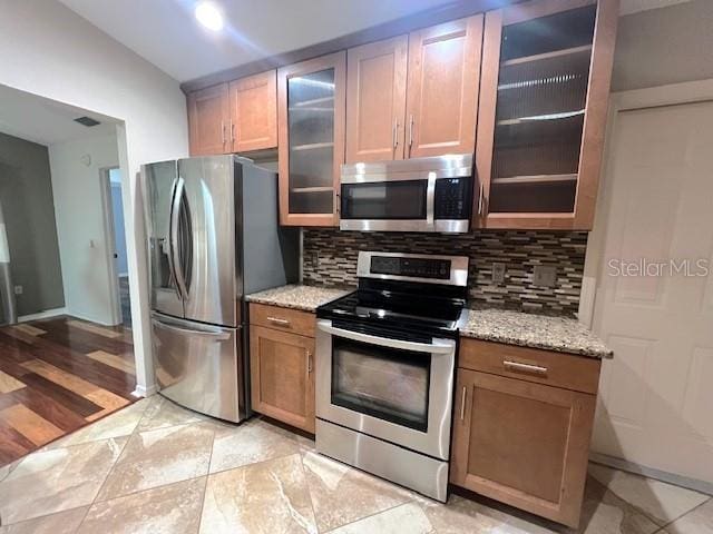 kitchen with light stone counters, decorative backsplash, vaulted ceiling, and stainless steel appliances