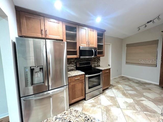 kitchen with tasteful backsplash, light stone countertops, stainless steel appliances, and rail lighting