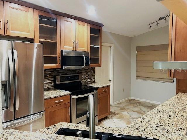 kitchen featuring tasteful backsplash, appliances with stainless steel finishes, light stone countertops, and vaulted ceiling