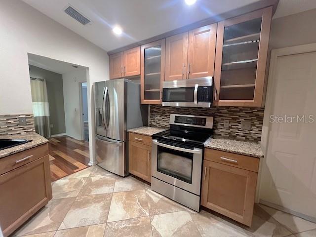 kitchen with light stone countertops, appliances with stainless steel finishes, lofted ceiling, and decorative backsplash