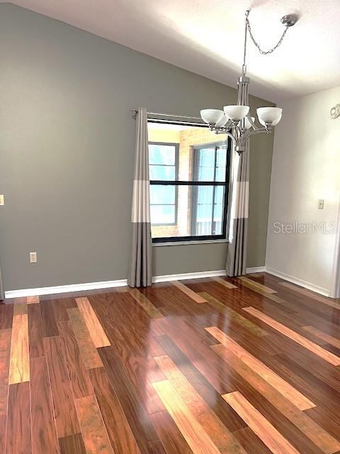 empty room with lofted ceiling, dark hardwood / wood-style floors, and a chandelier