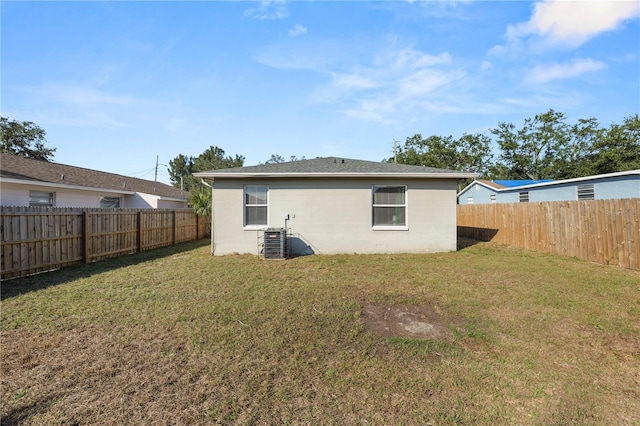 rear view of house with central AC unit and a lawn