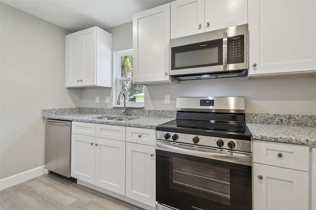 kitchen featuring sink, white cabinetry, light stone counters, light wood-type flooring, and stainless steel appliances