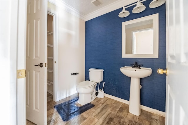 bathroom with visible vents, toilet, ornamental molding, a sink, and wood finished floors