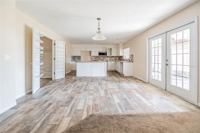 kitchen with a sink, decorative backsplash, french doors, white cabinetry, and stainless steel microwave