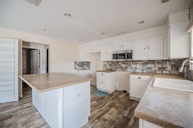 kitchen with a sink, stainless steel microwave, backsplash, wood finished floors, and white cabinetry