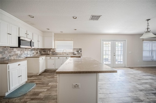 kitchen featuring visible vents, stainless steel microwave, a kitchen island, french doors, and a sink