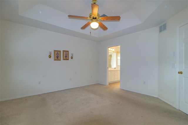 spare room with light carpet, a tray ceiling, and ceiling fan