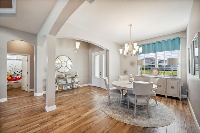 dining room featuring arched walkways, a notable chandelier, light wood-style flooring, and baseboards