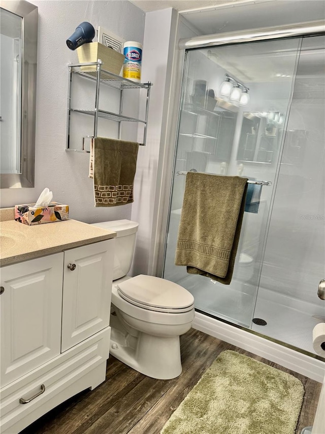 bathroom with wood-type flooring, toilet, a shower with door, and vanity