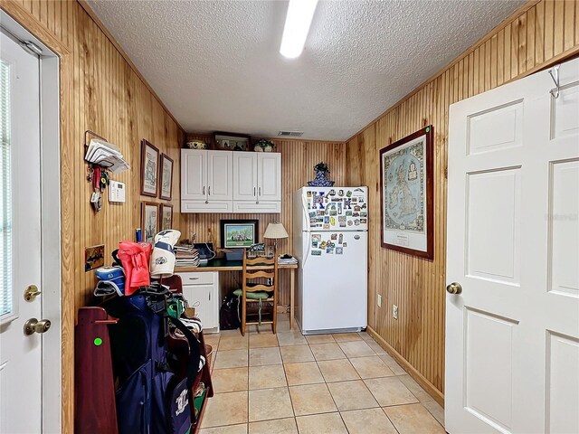 laundry area featuring wood walls, a textured ceiling, and light tile patterned floors