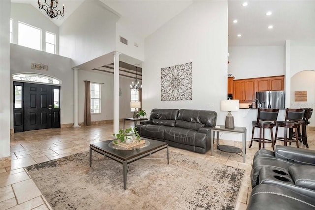 living area with stone tile floors, a notable chandelier, visible vents, baseboards, and decorative columns