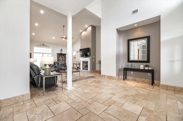 interior space with decorative columns, stone tile floors, visible vents, ceiling fan, and high vaulted ceiling