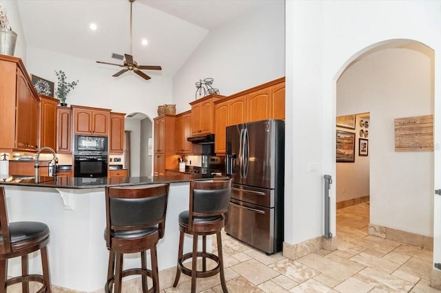 kitchen featuring arched walkways, high vaulted ceiling, a peninsula, a kitchen breakfast bar, and black appliances