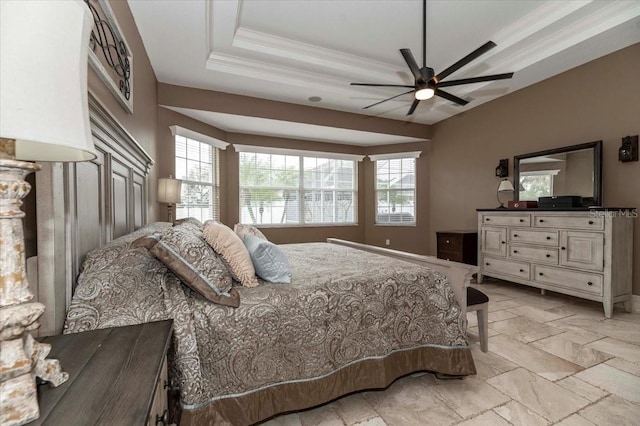 bedroom with a ceiling fan, stone tile flooring, a raised ceiling, and crown molding