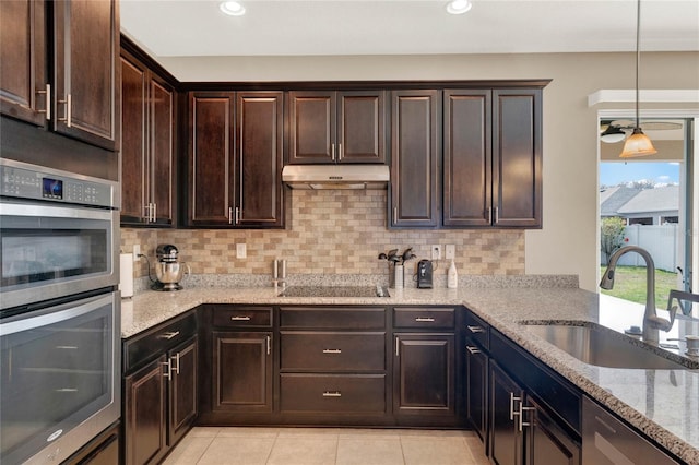 kitchen featuring dark brown cabinets, sink, stainless steel double oven, and light stone counters