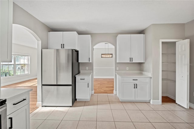 kitchen with white cabinetry, light stone countertops, stainless steel refrigerator, and light tile patterned flooring