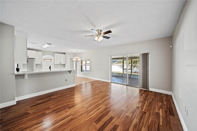 unfurnished living room featuring sink, hardwood / wood-style flooring, ceiling fan with notable chandelier, and a textured ceiling