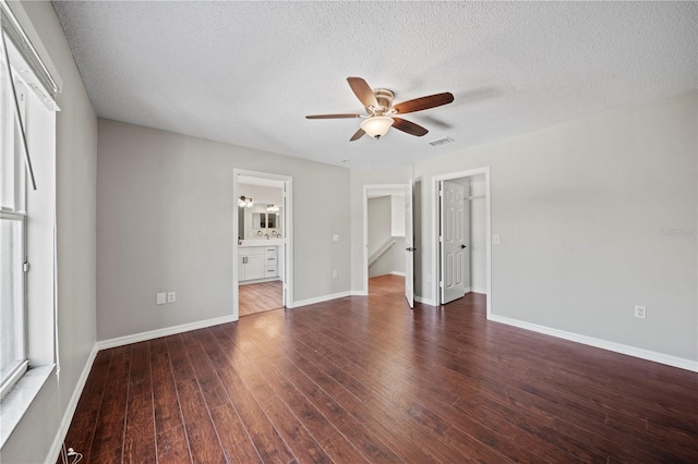 unfurnished bedroom featuring ensuite bath, dark wood-type flooring, ceiling fan, a textured ceiling, and a spacious closet