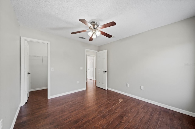 unfurnished bedroom with dark hardwood / wood-style floors, a spacious closet, ceiling fan, a textured ceiling, and a closet