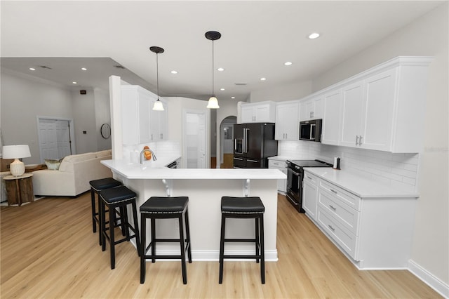 kitchen with decorative light fixtures, black appliances, white cabinets, a kitchen breakfast bar, and kitchen peninsula