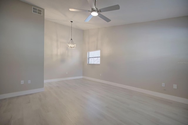 empty room with ceiling fan with notable chandelier and light wood-type flooring