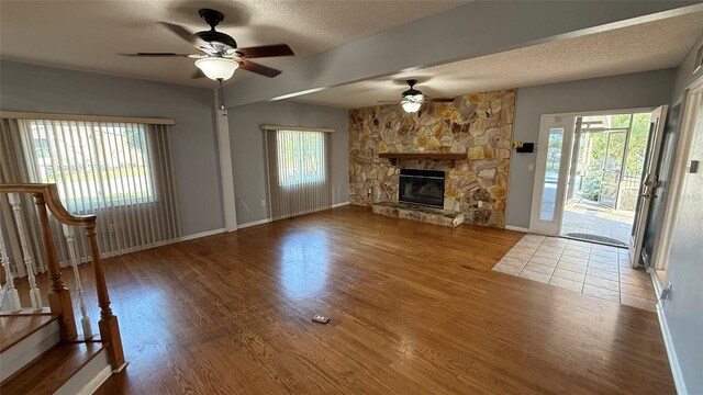 unfurnished living room with hardwood / wood-style flooring, a stone fireplace, and a textured ceiling