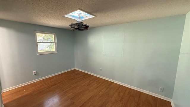 unfurnished room featuring a skylight, hardwood / wood-style floors, and a textured ceiling