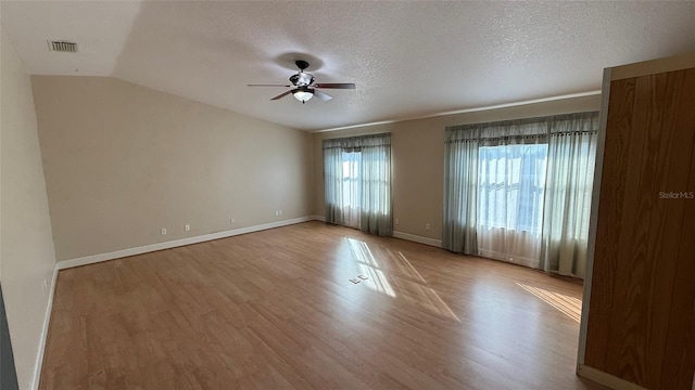 empty room with vaulted ceiling, ceiling fan, a textured ceiling, and light hardwood / wood-style floors