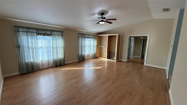 spare room with ceiling fan, vaulted ceiling, light hardwood / wood-style floors, and a textured ceiling