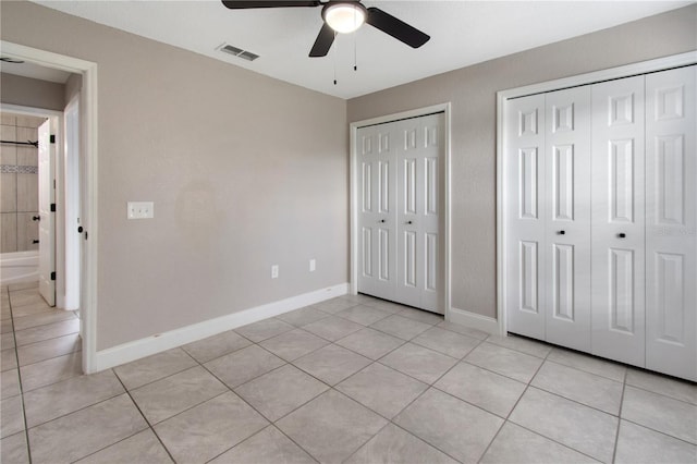 unfurnished bedroom with light tile patterned flooring, two closets, and ceiling fan