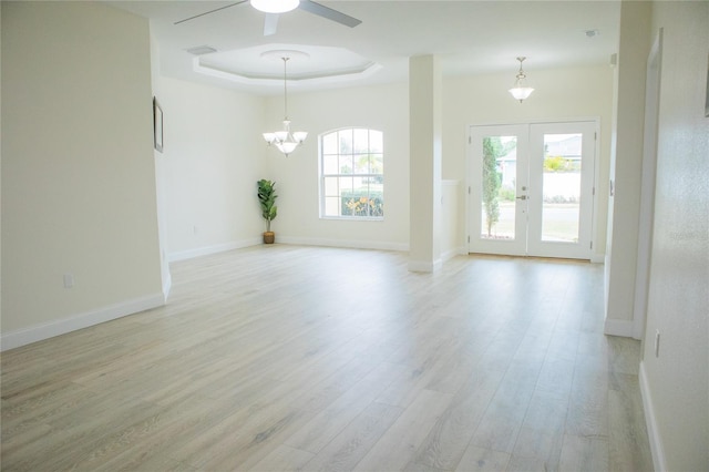 unfurnished room with a tray ceiling, ceiling fan with notable chandelier, light hardwood / wood-style floors, and french doors