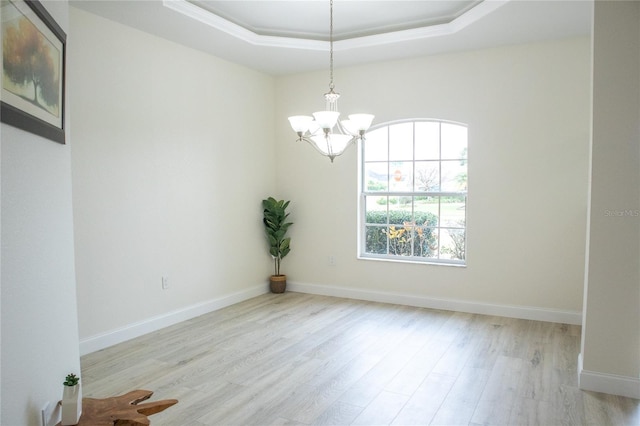 empty room featuring light hardwood / wood-style flooring, a raised ceiling, and a chandelier