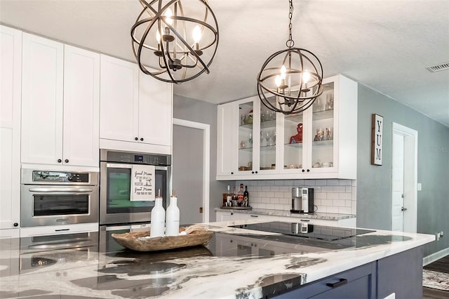 kitchen with black electric stovetop, light stone countertops, a chandelier, and white cabinets