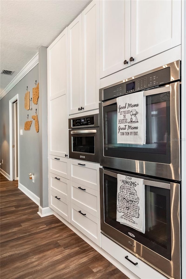 kitchen featuring dark wood-type flooring, ornamental molding, white cabinets, a textured ceiling, and stainless steel double oven