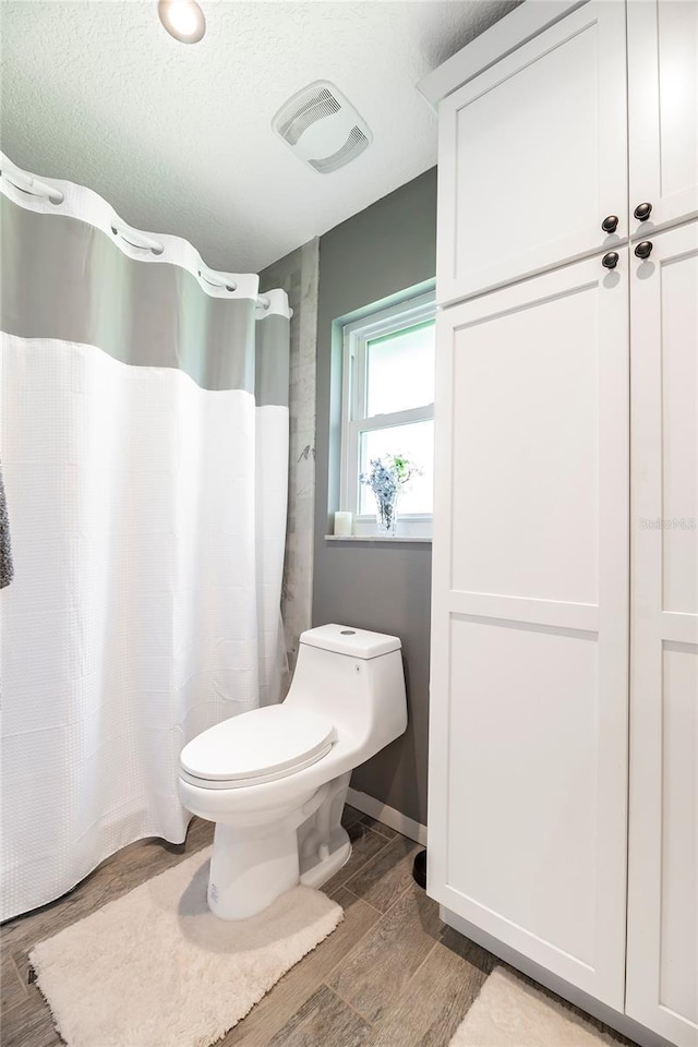 full bathroom featuring toilet, a shower with shower curtain, wood finished floors, visible vents, and baseboards