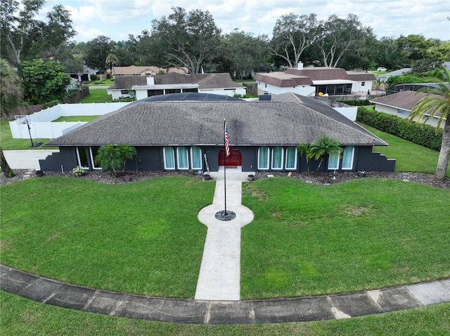 ranch-style home featuring a shingled roof, fence, and a front lawn