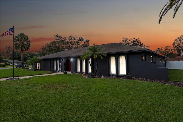 view of front of property with stucco siding, a lawn, and fence