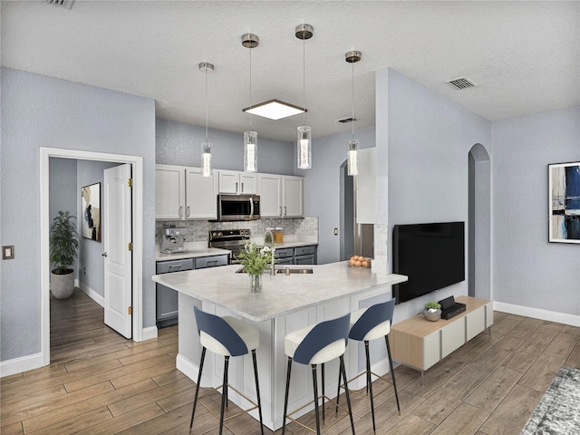 kitchen with pendant lighting, white cabinetry, backsplash, stainless steel appliances, and a kitchen bar