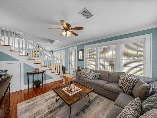 living room with wood-type flooring, ornamental molding, ceiling fan, and a textured ceiling