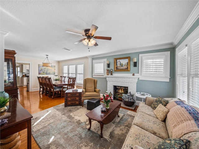 living room with hardwood / wood-style flooring, ceiling fan, ornamental molding, a textured ceiling, and a brick fireplace