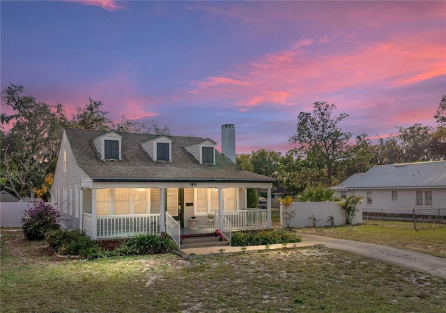 cape cod house featuring covered porch and a lawn