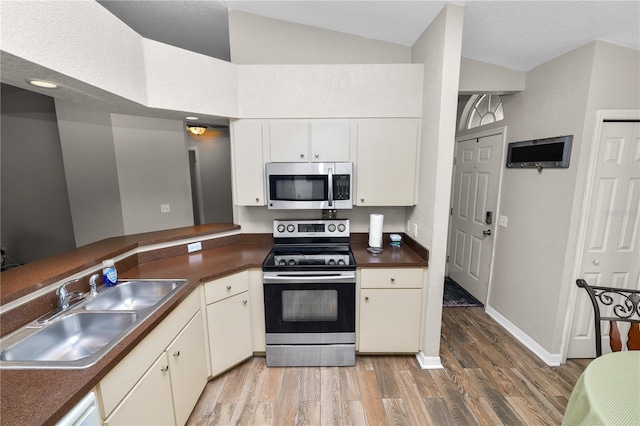 kitchen with sink, white cabinetry, vaulted ceiling, appliances with stainless steel finishes, and hardwood / wood-style floors