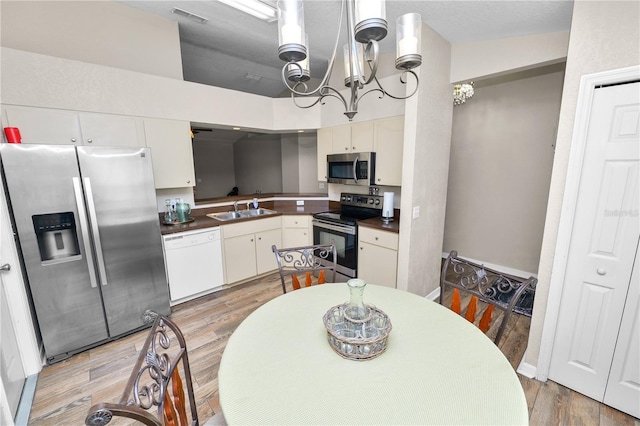 kitchen with wood-type flooring, white cabinetry, sink, a notable chandelier, and stainless steel appliances