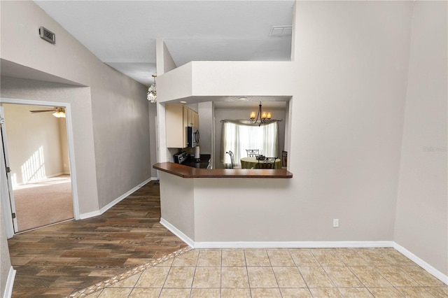 kitchen featuring sink, stove, hanging light fixtures, ceiling fan with notable chandelier, and kitchen peninsula