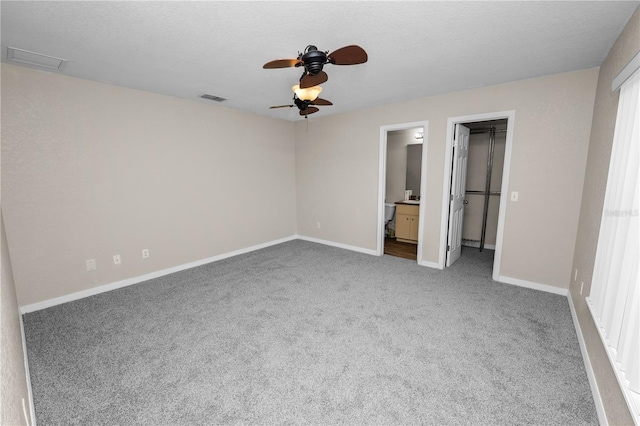 unfurnished bedroom featuring ensuite bathroom, carpet floors, a spacious closet, ceiling fan, and a textured ceiling