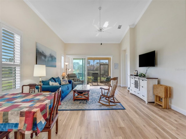 living room with crown molding, light hardwood / wood-style flooring, ceiling fan, and a high ceiling