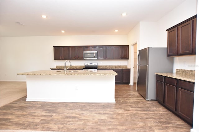 kitchen featuring dark brown cabinetry, sink, a center island with sink, appliances with stainless steel finishes, and light stone countertops