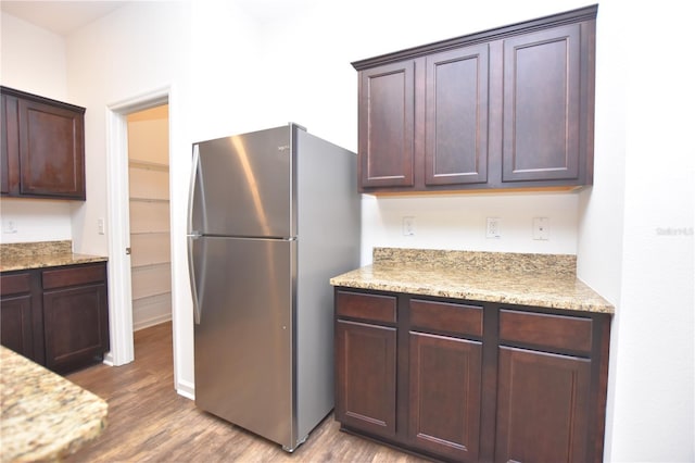 kitchen with light stone counters, hardwood / wood-style flooring, stainless steel fridge, and dark brown cabinets