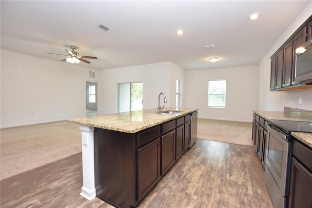 kitchen with sink, stainless steel appliances, dark brown cabinetry, light stone countertops, and a center island with sink